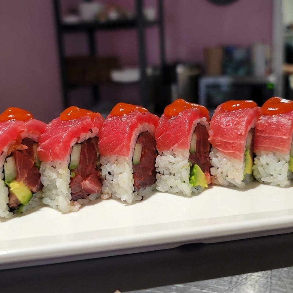 Row of tuna sushi rolls topped with red sauce, served on a white rectangular plate with wasabi.