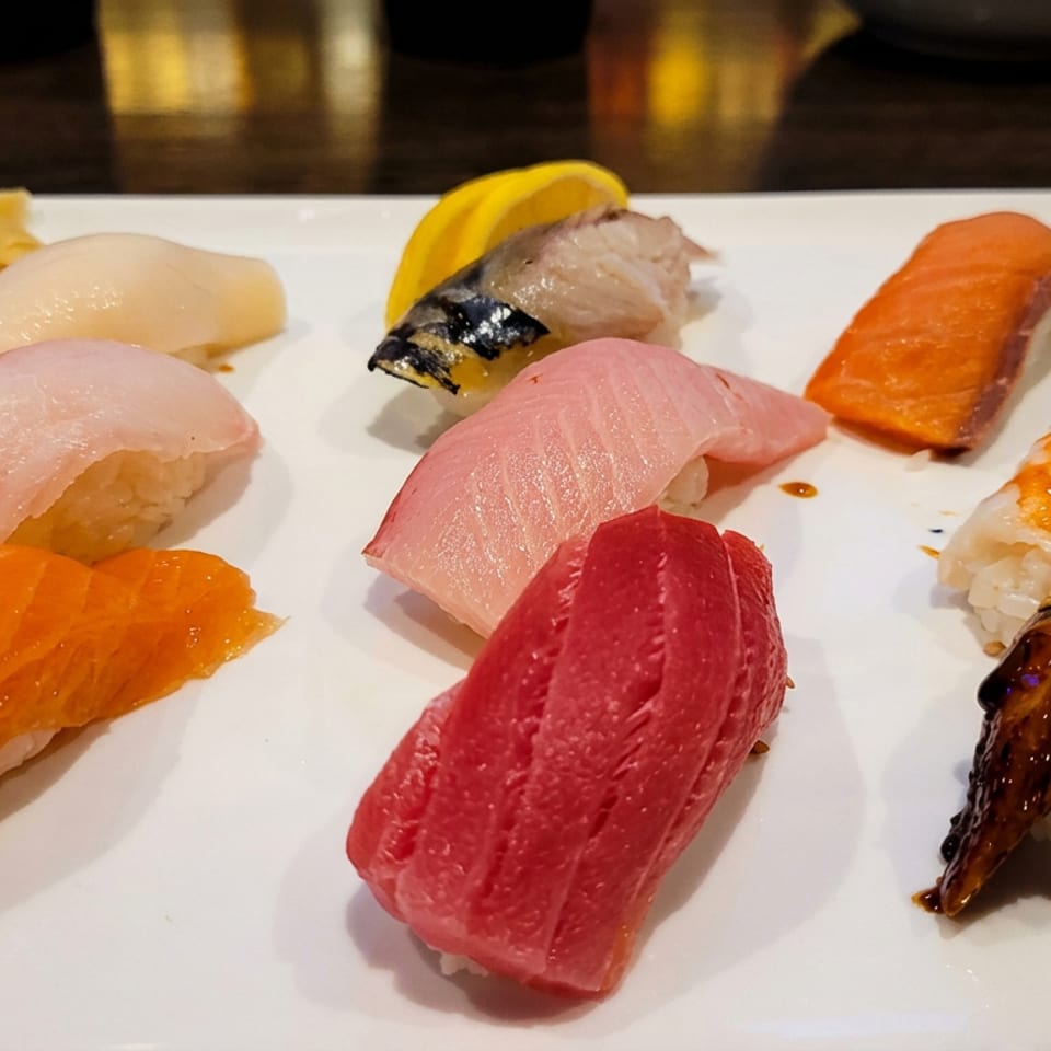 Assorted sushi nigiri, including salmon, tuna, white fish, shrimp, and eel, arranged on a white rectangular plate.