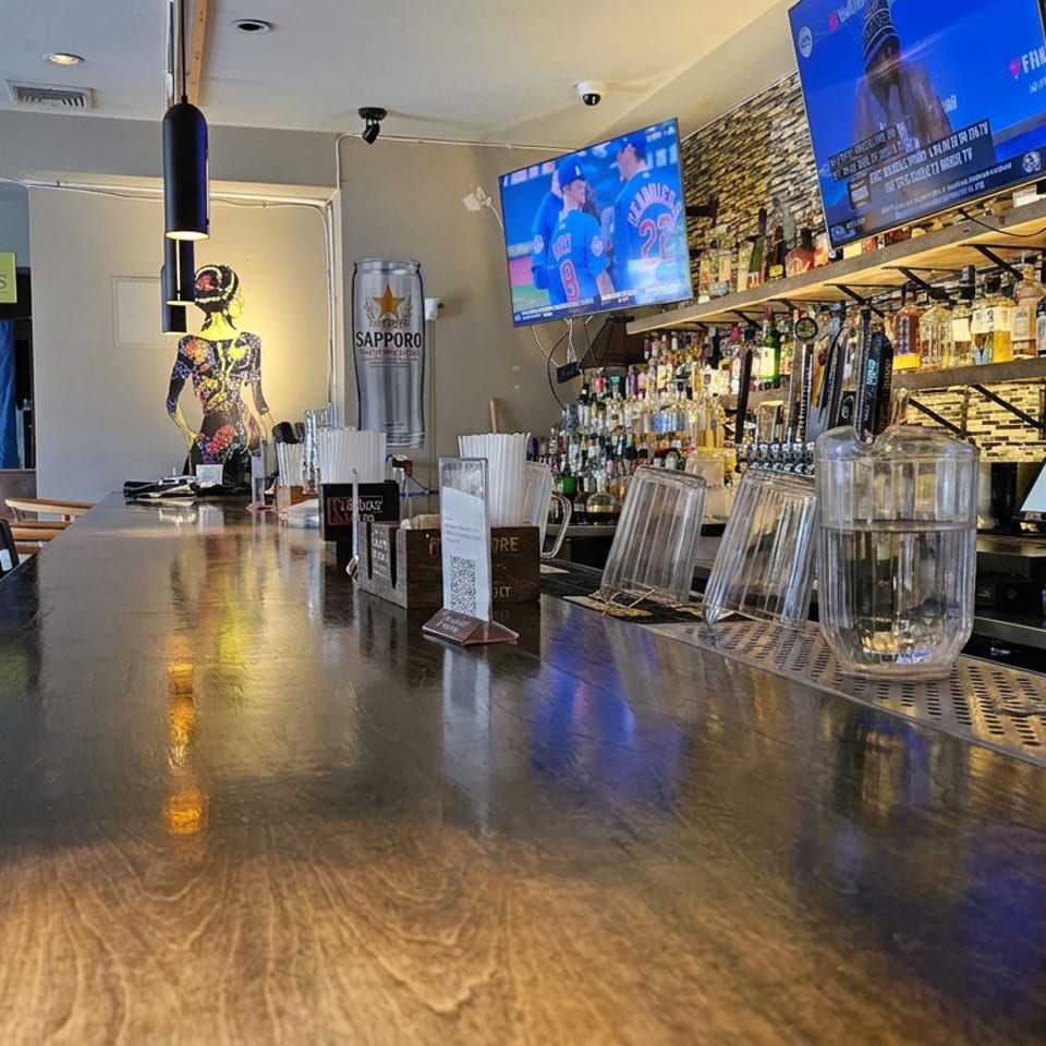 Empty restaurant bar with polished wooden counter, liquor shelves, TVs showing sports, and Sapporo beer branding.