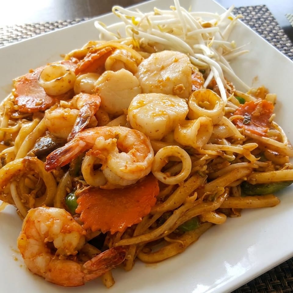 Plate of stir-fried noodles topped with shrimp, squid, scallops, crab, vegetables, and bean sprouts.