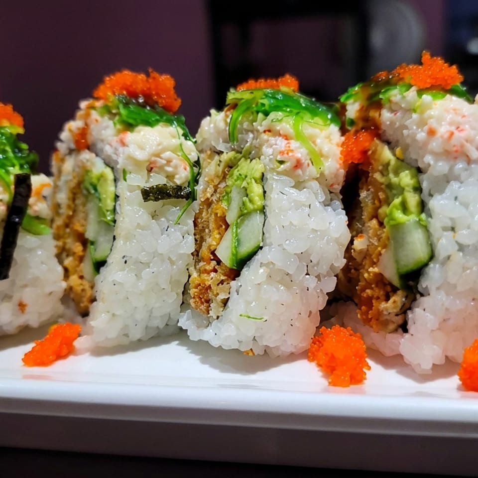 Close-up of assorted sushi rolls topped with orange roe, seaweed, avocado, cucumber, and crispy coating on a white platter.