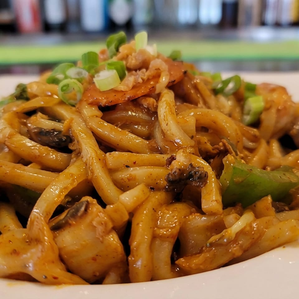 Plate of saucy seafood pasta with mussels, shrimp, vegetables, and green onions in a restaurant setting.